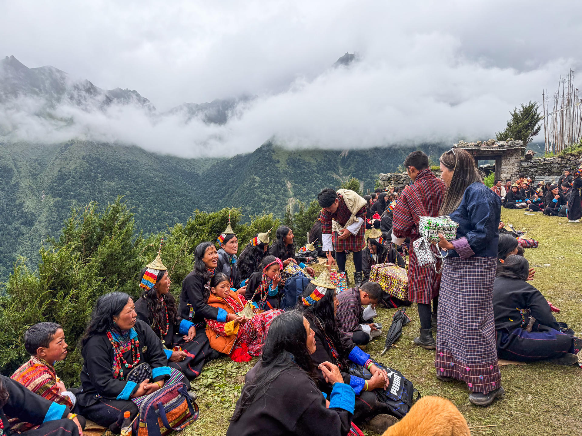 A group of people in traditional attire gathered on a hillside with mountains in the background.