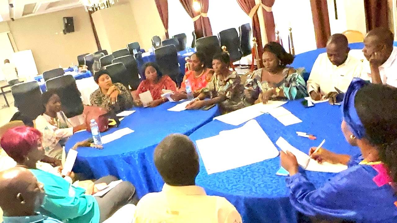 Group of people seated around a round table covered with a blue cloth, engaging in discussion.