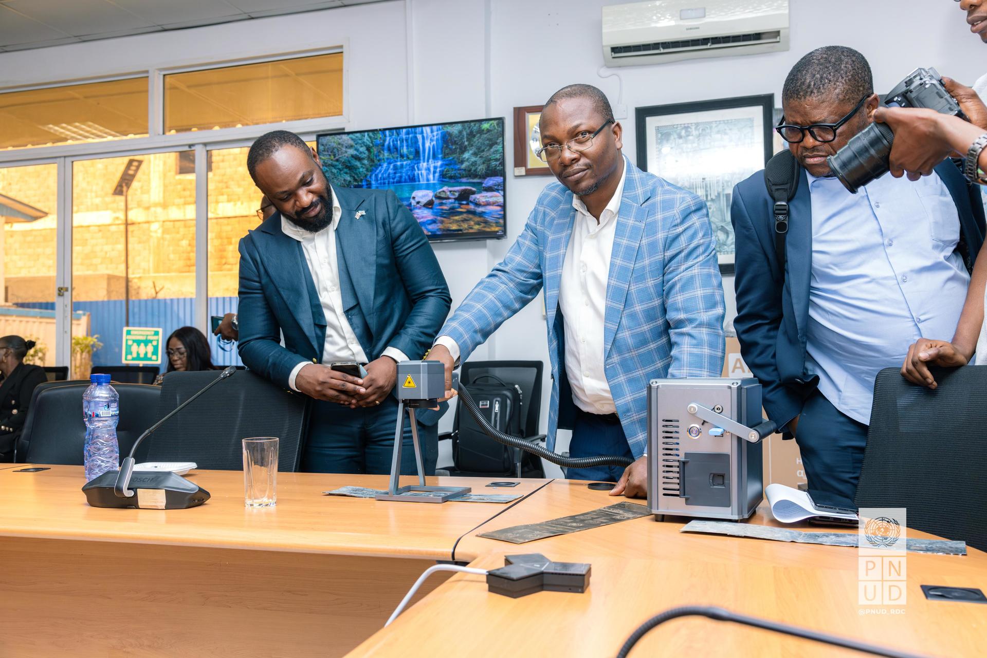 Four men gathered around a conference table, examining a device in a meeting room.