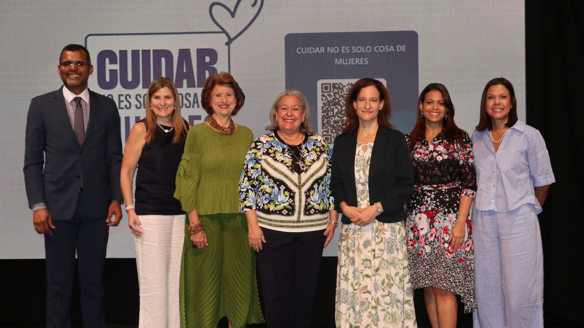 Un grupo de siete personas sonriendo juntas en el escenario, con un fondo de presentación