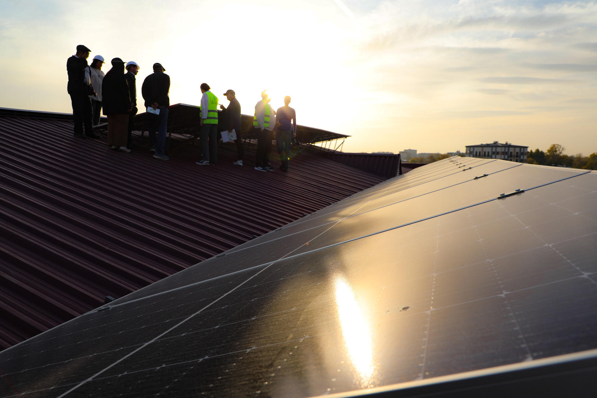 Group of people on a roof at sunset, with solar panels reflecting light.