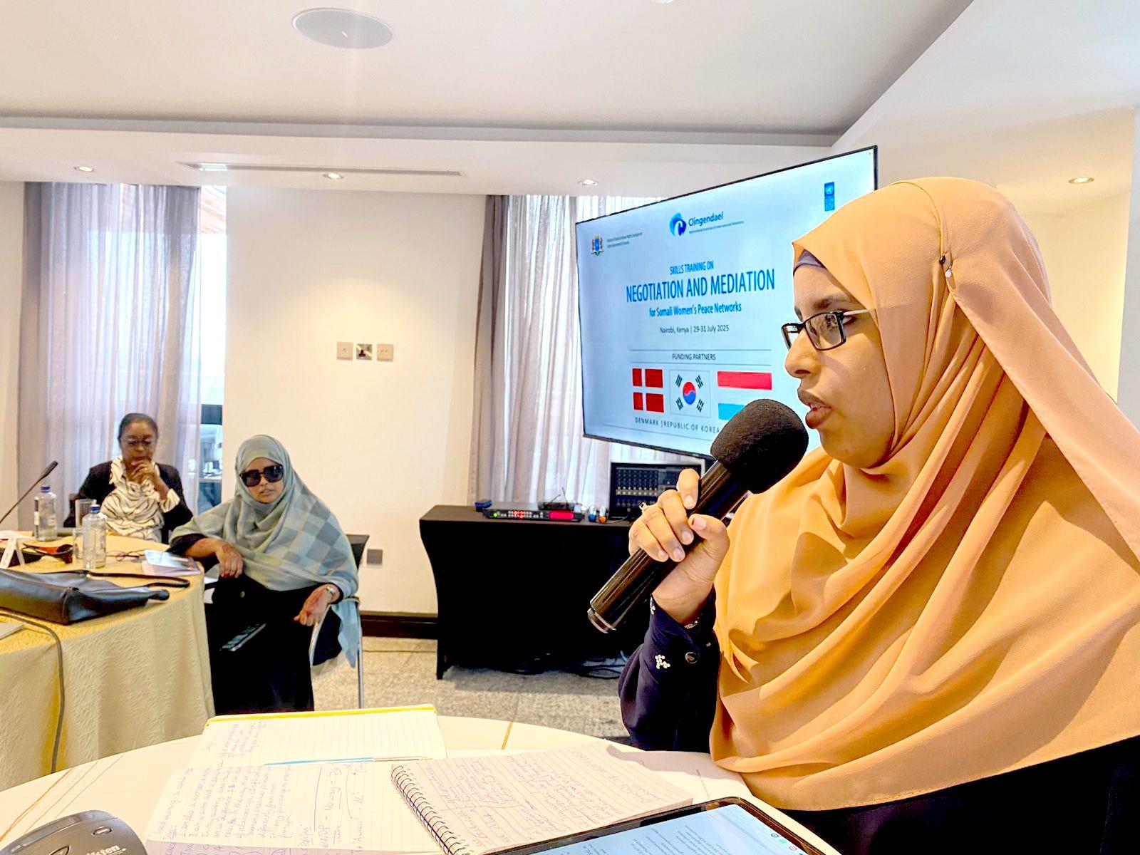 A woman in a hijab speaks into a microphone during a conference with participants in the background.Somali Women’s Peace Network has shifted norms, cemented women’s place in peacebuilding: Madina Ahmed Nur