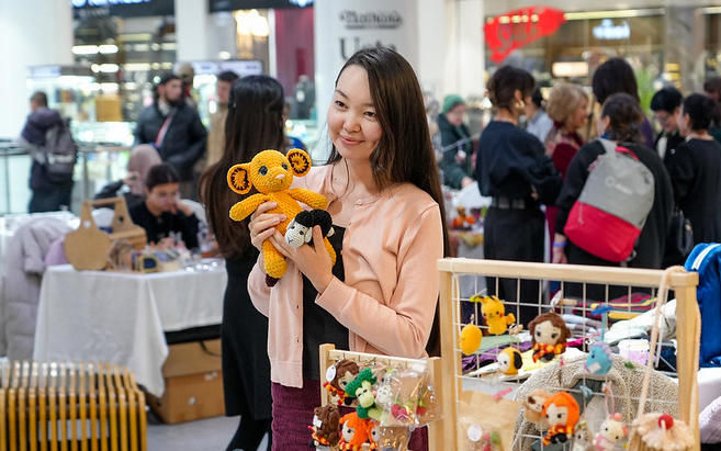 Young woman smiling while holding a plush toy at a market with people in the background.