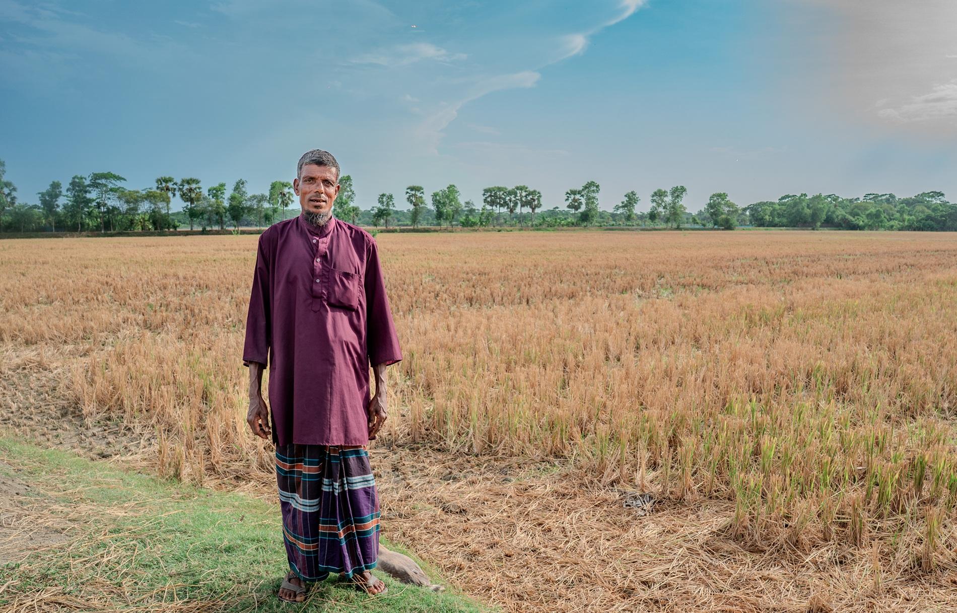 A man in a traditional outfit stands in a golden field under a blue sky.