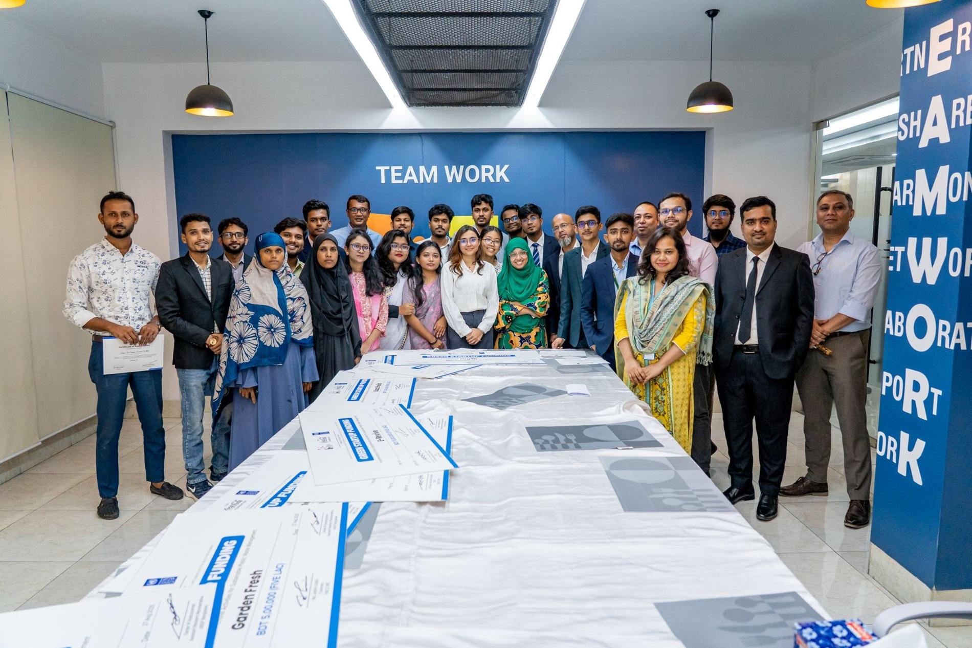 A large group of diverse professionals poses together around a table in a modern office.