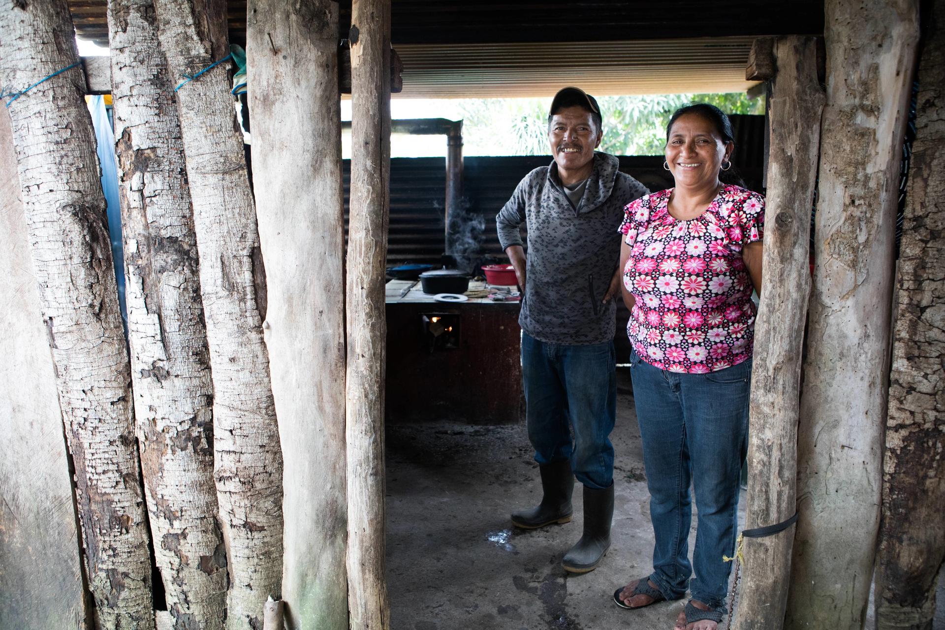 A man and woman smile together in an open doorway framed by wooden posts.