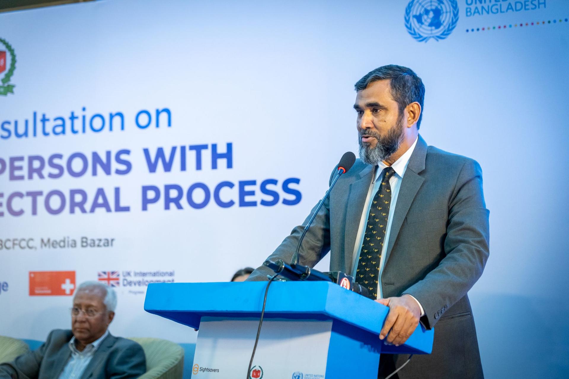 A speaker at a consultation event stands at a podium, addressing an audience.