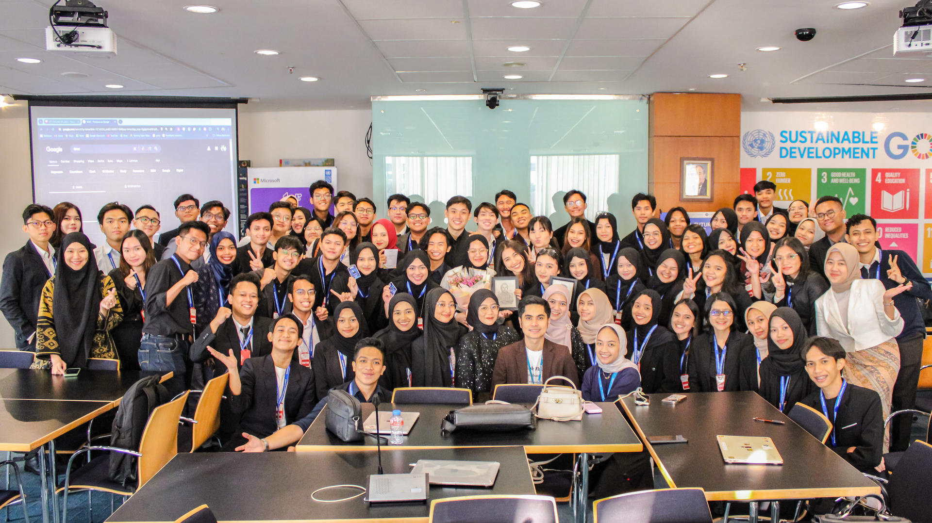 A large group of diverse students in formal attire poses together in a classroom setting.
