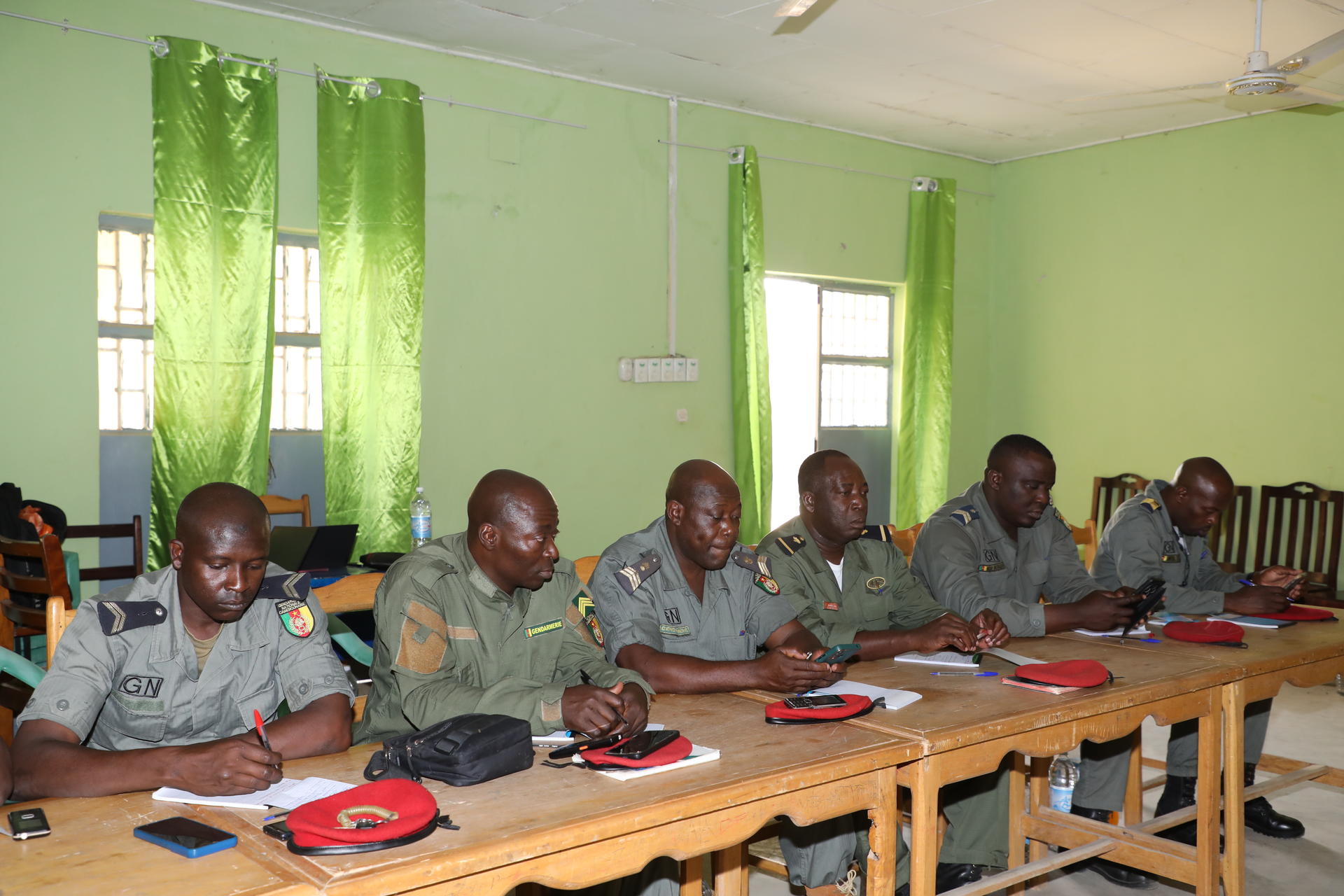Group of men seated at a long table in a bright green room, red folders in front.