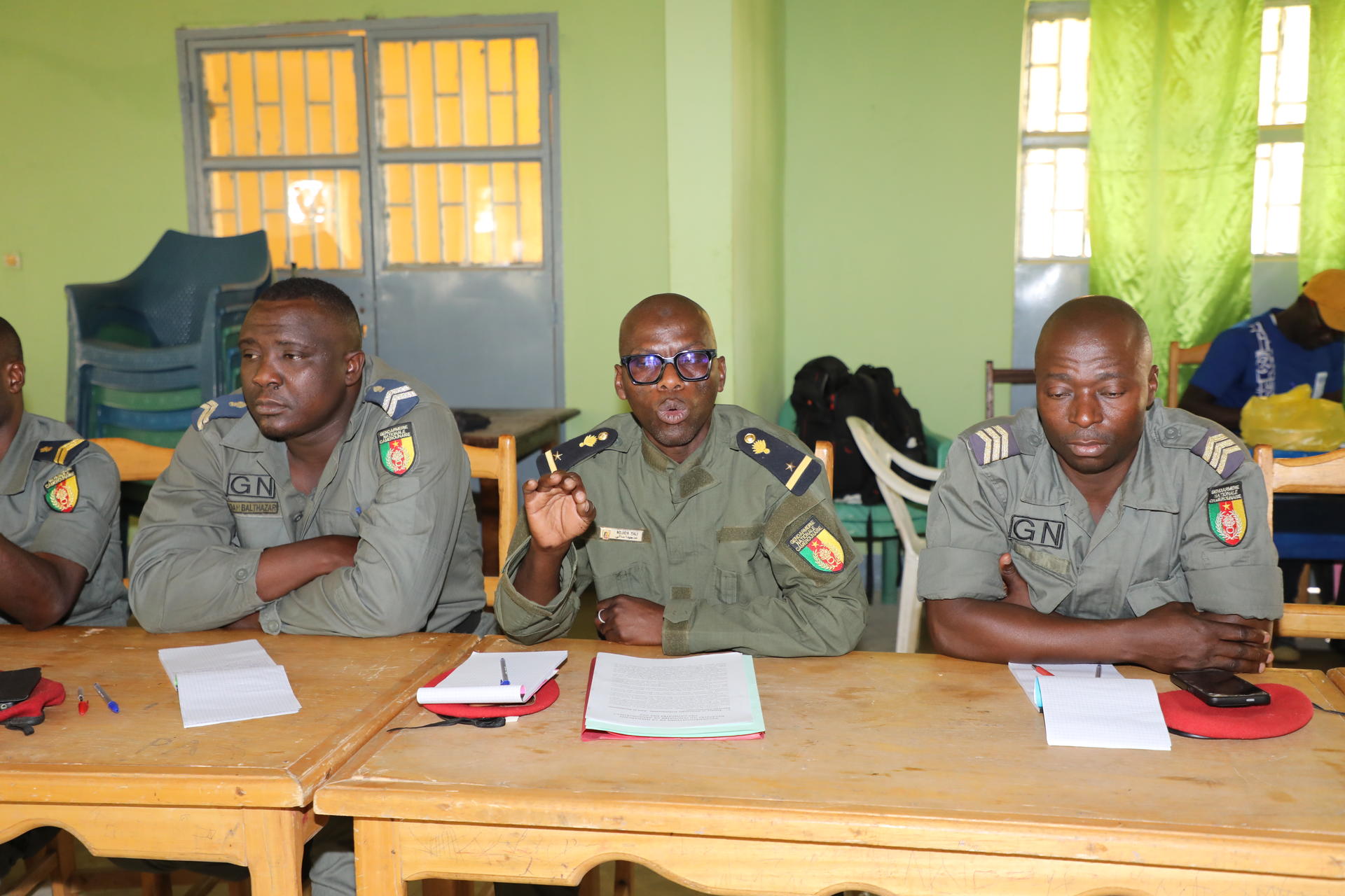Four uniformed men sit at a wooden table with papers in a bright green room.