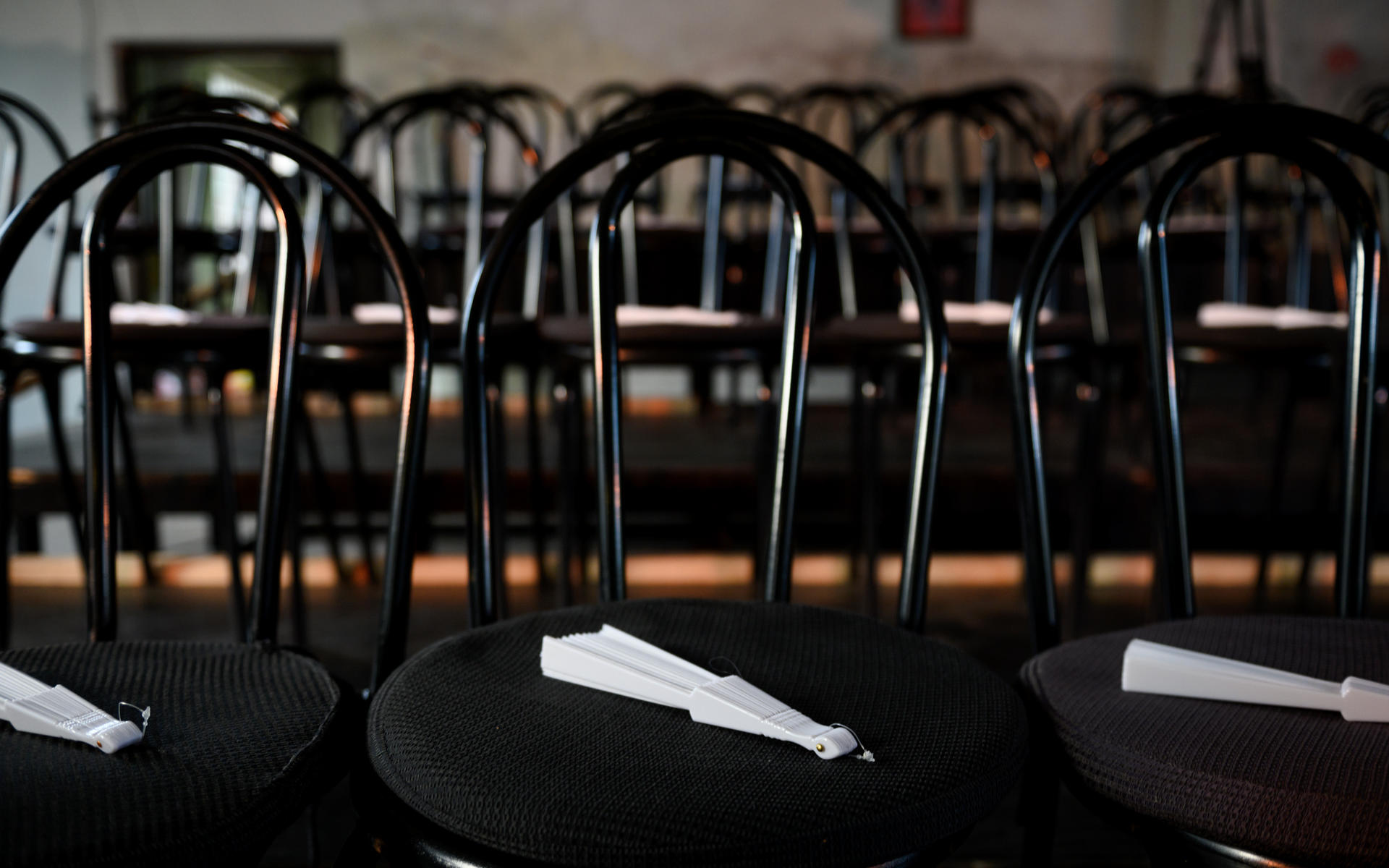 Row of black metal chairs with folded white napkins on seats in a dim dining room.