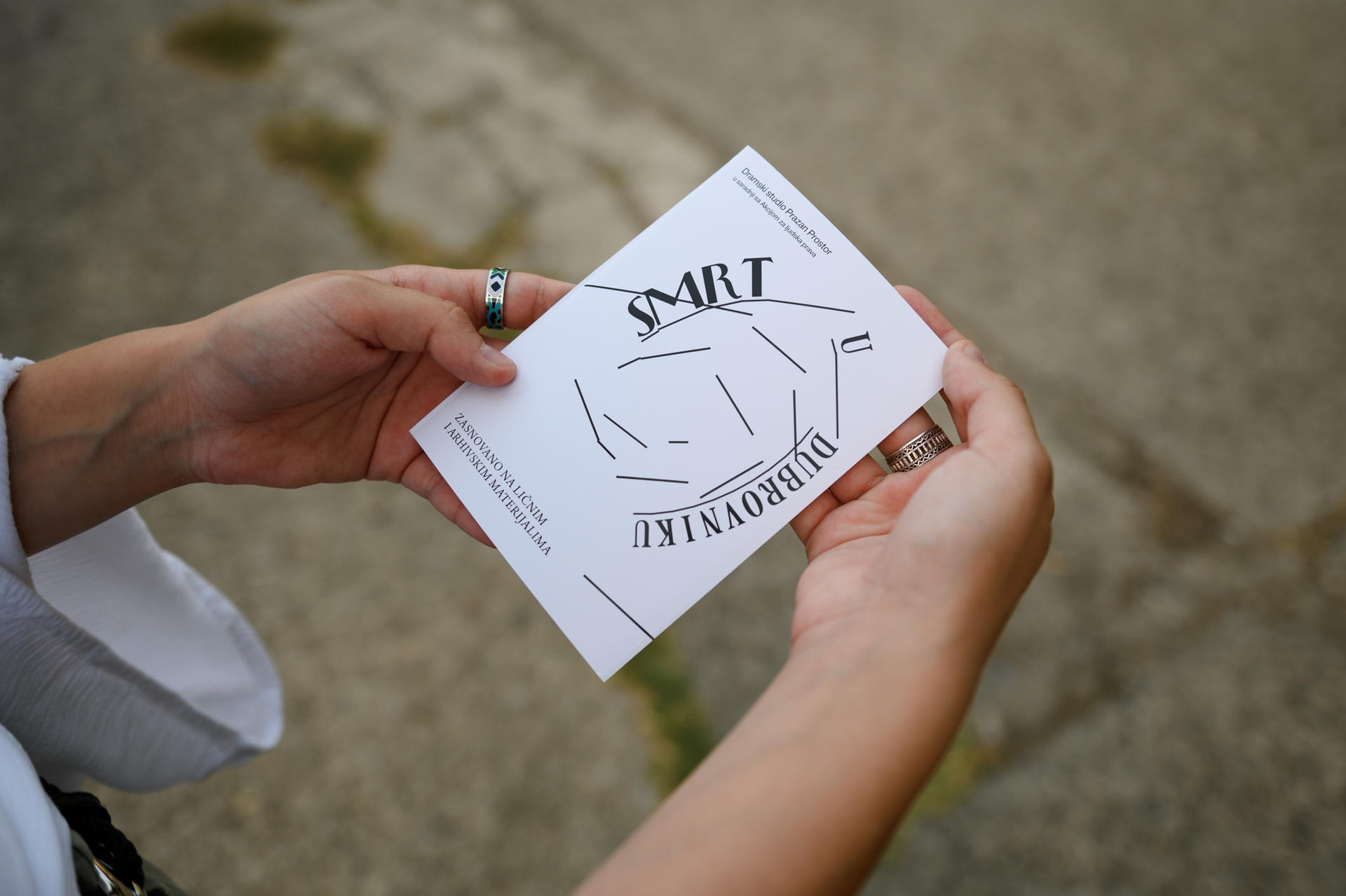 Hands hold a white folded card with the SALT logo outdoors on a gravel surface.