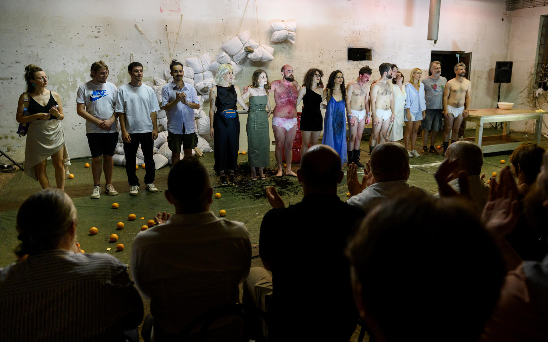 Group of people standing in a line on a stage, facing an audience in a dimly lit hall.