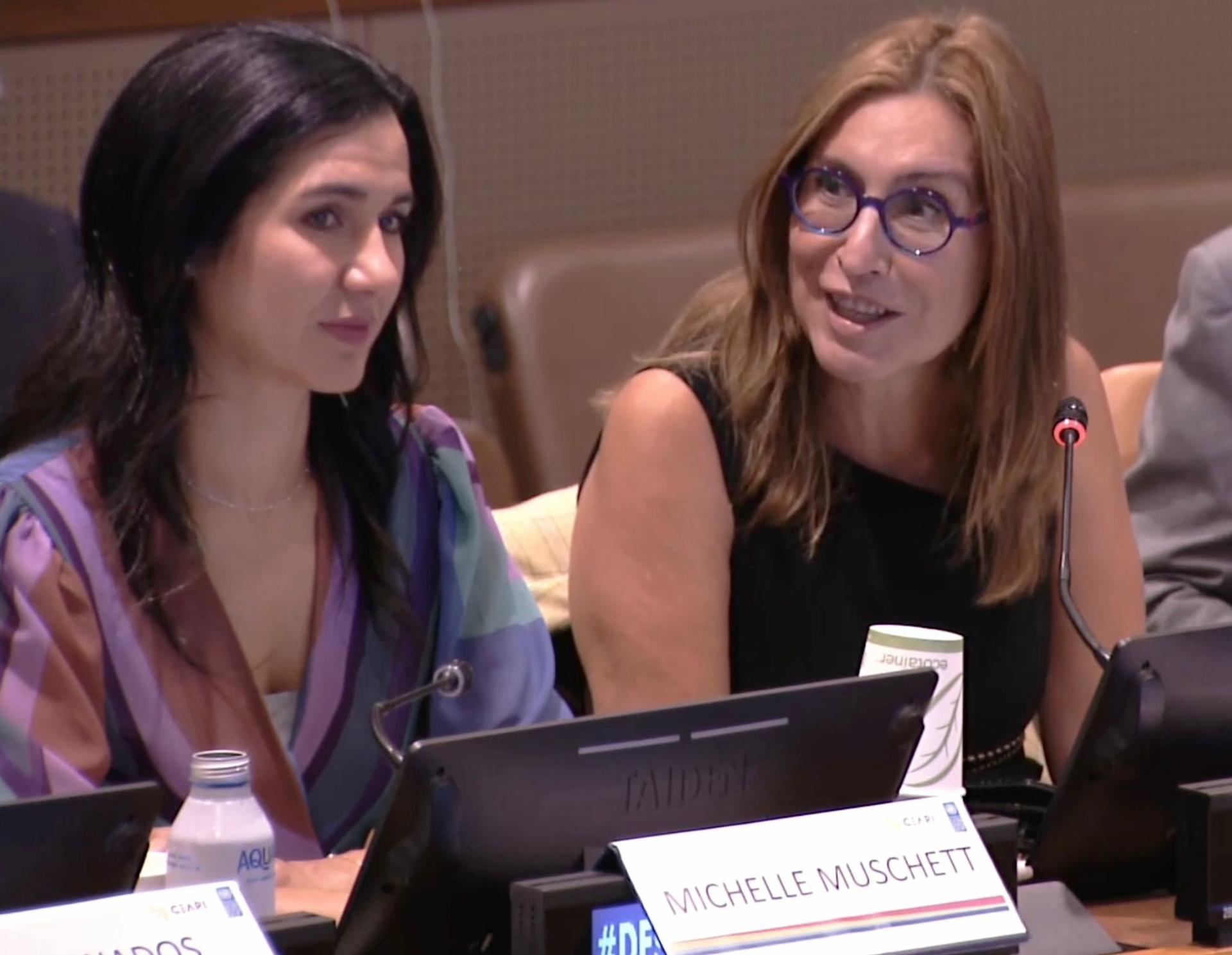 Two women at a panel discussion with microphones and tablets.