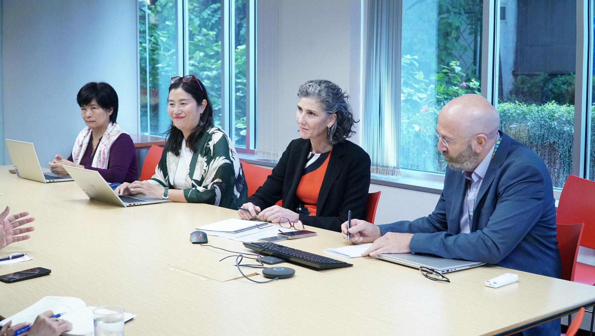 Five professionals sit around a bright conference table in a boardroom, with notebooks and a laptop.