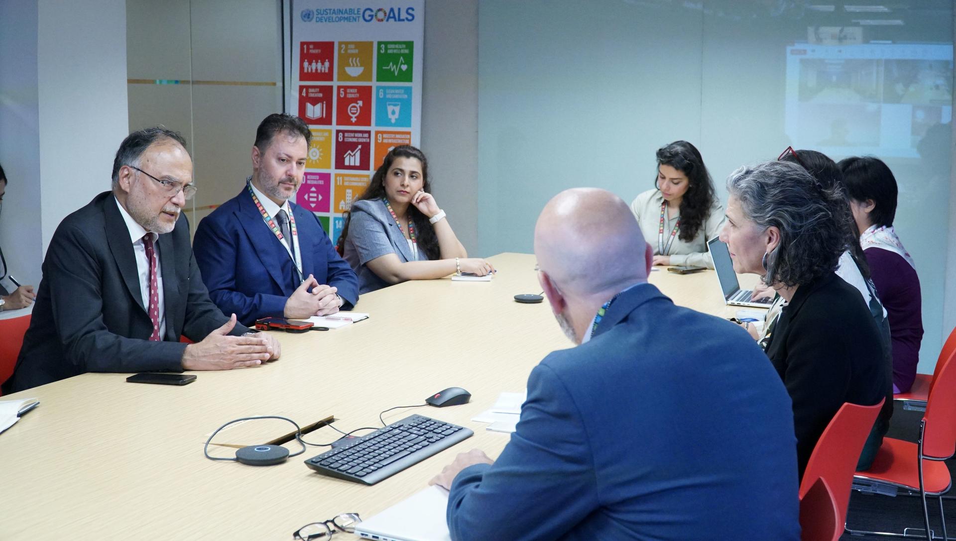 Group of professionals in a boardroom meeting around a long table, speakerphone in the foreground.