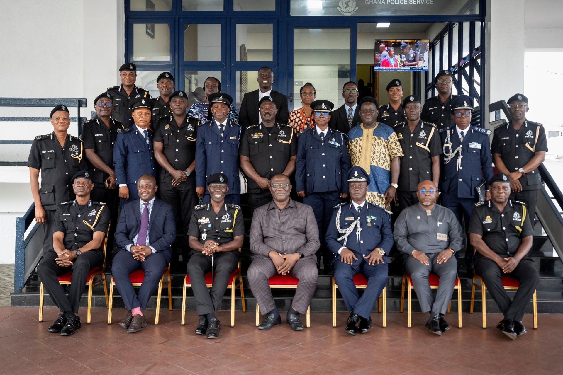 Group of uniformed officers and civilians posing on steps outside a blue-framed building.