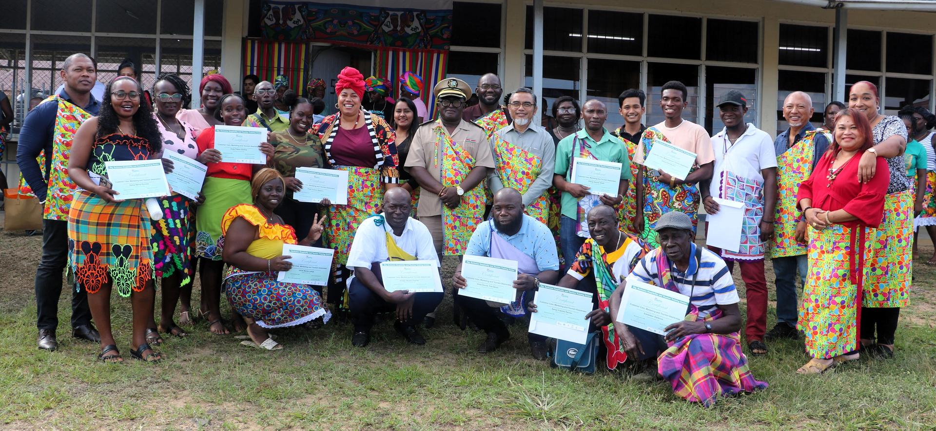 Smiling group posing with blue certificates outside a building in colorful attire.
