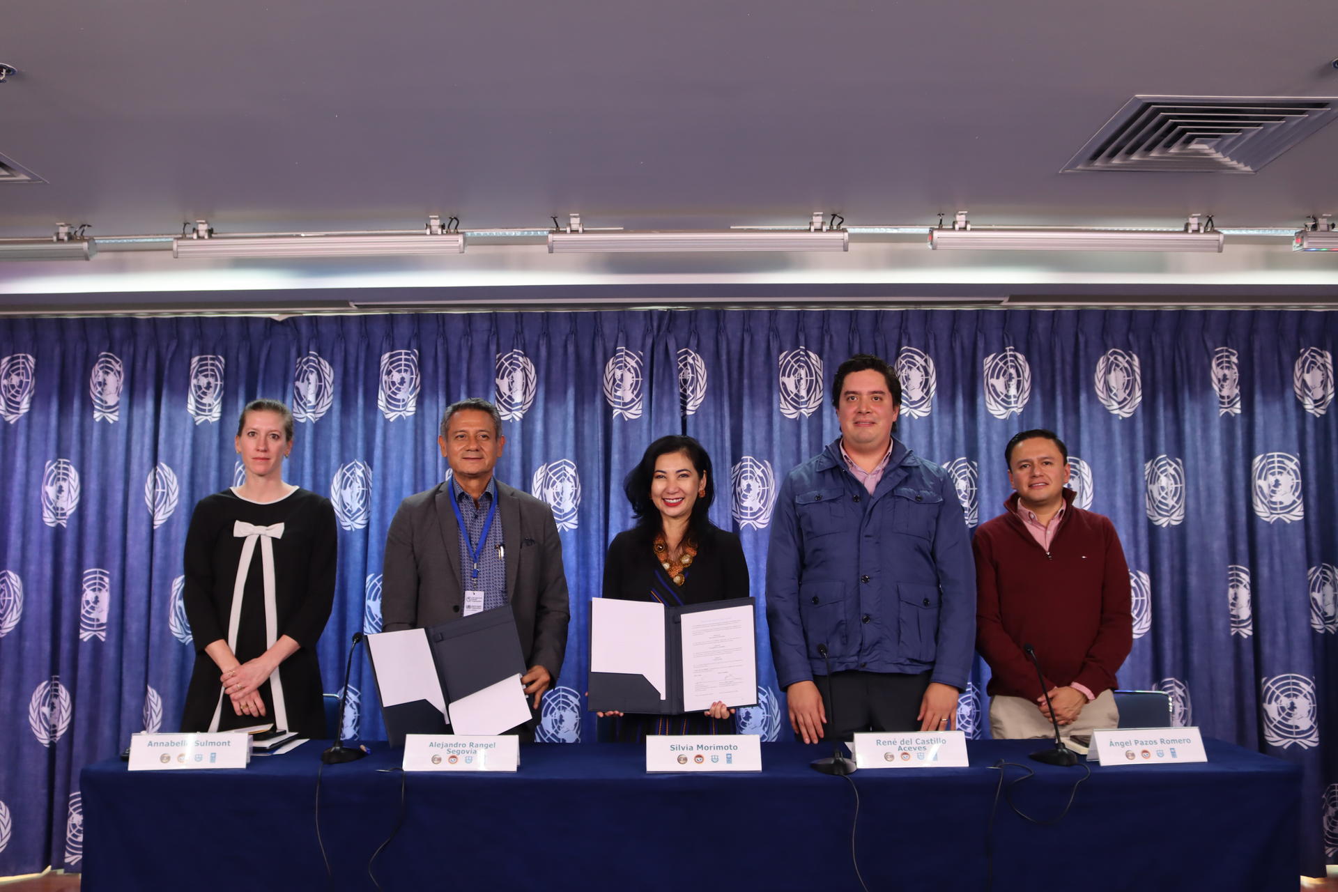 Five panelists sit behind a long table on a stage; blue backdrop with logos.