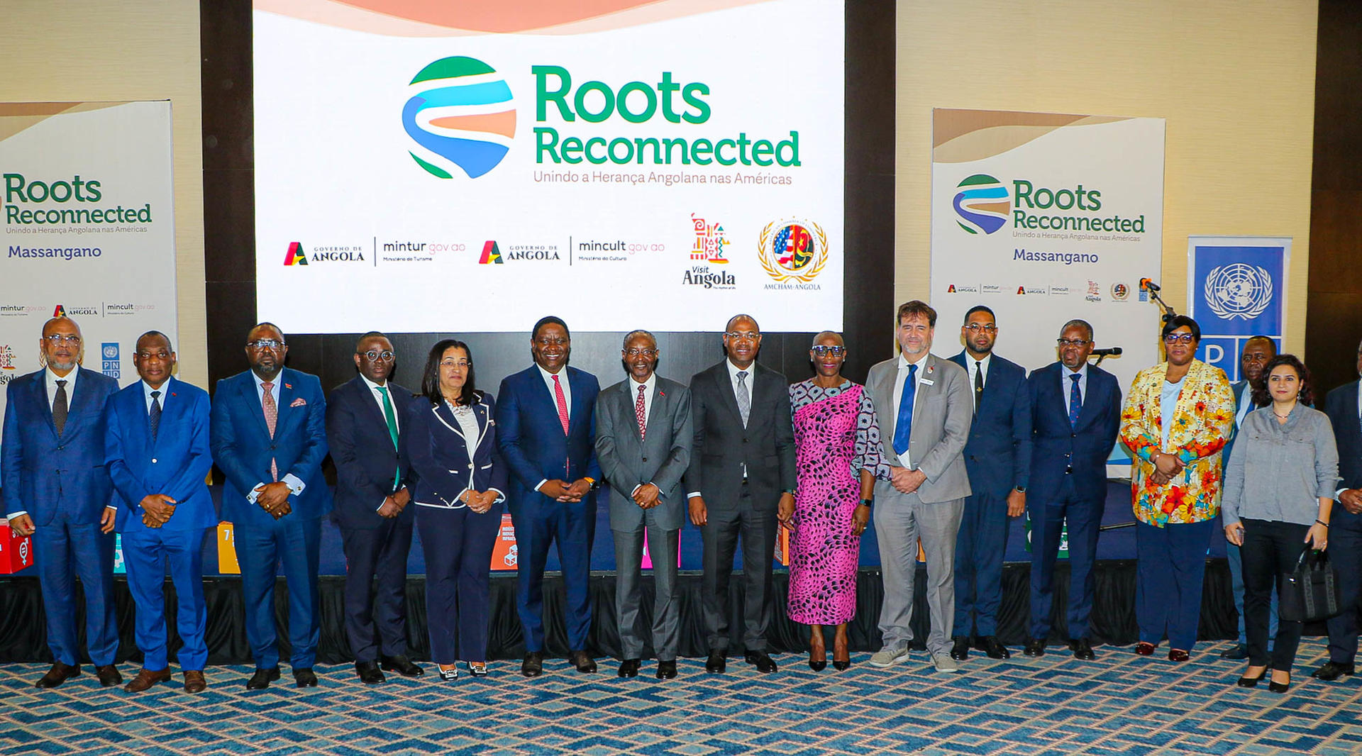 Photo: group of formally dressed people posing on stage at the Roots Reconnected conference.