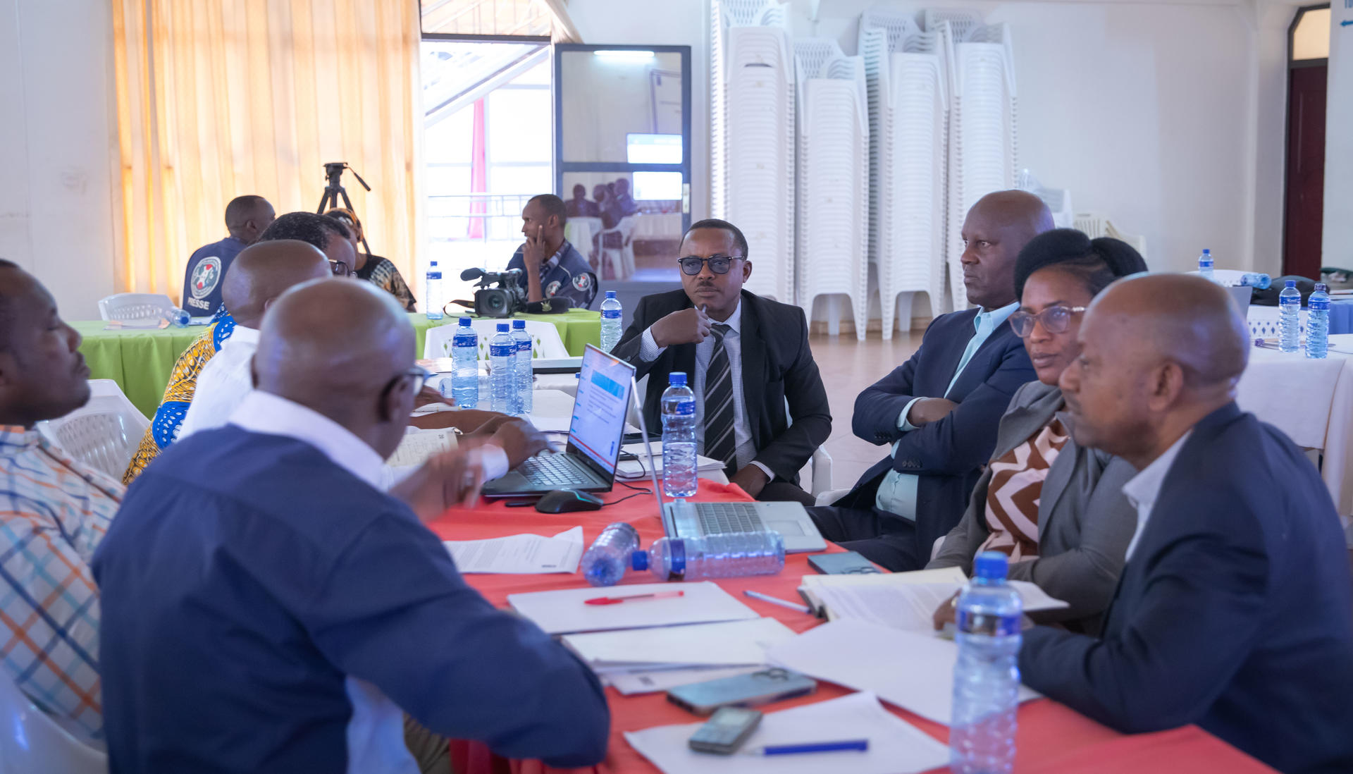 Professionally dressed attendees sit around a red-covered conference table, engaged in discussion.PNUD - vers un développement durable sensible aux risques climatiques et aux catastrophes