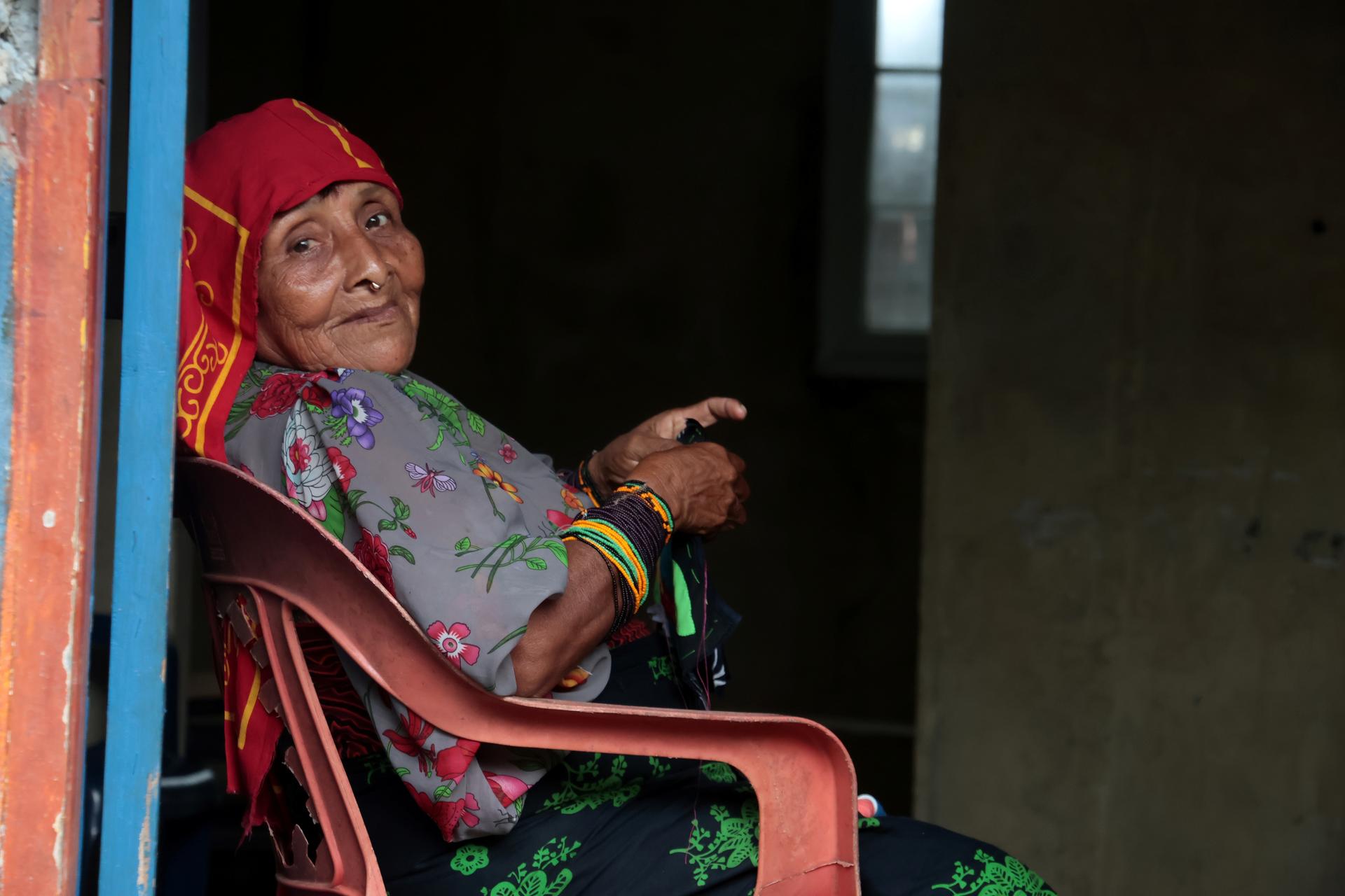 Una mujer indìgena con vestido colorido está sentada sonriendo hacia el frente