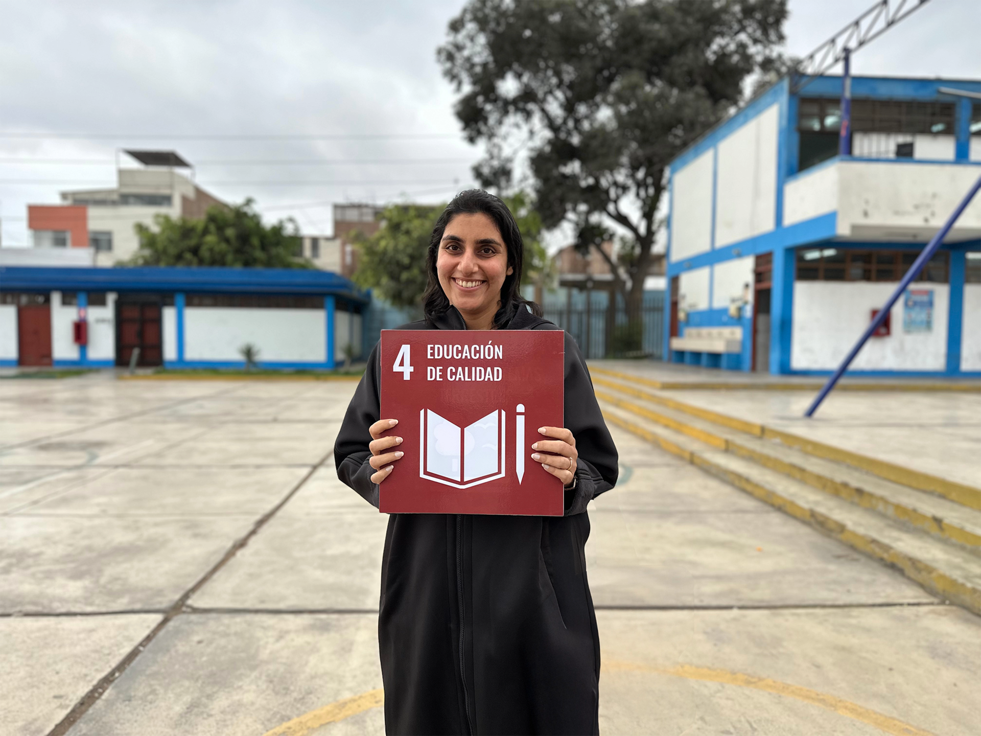 Female with a black coat is holding the SDG 4 sign in a schoolyard