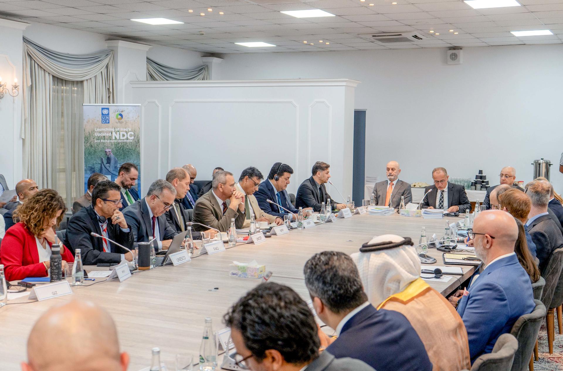 Diverse group in a well-lit conference room sits around a long table in discussion.