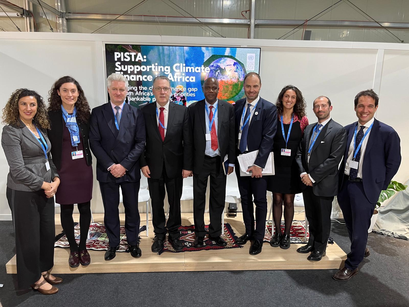 Group of professionals in suits posing at a trade show booth with blue banners.