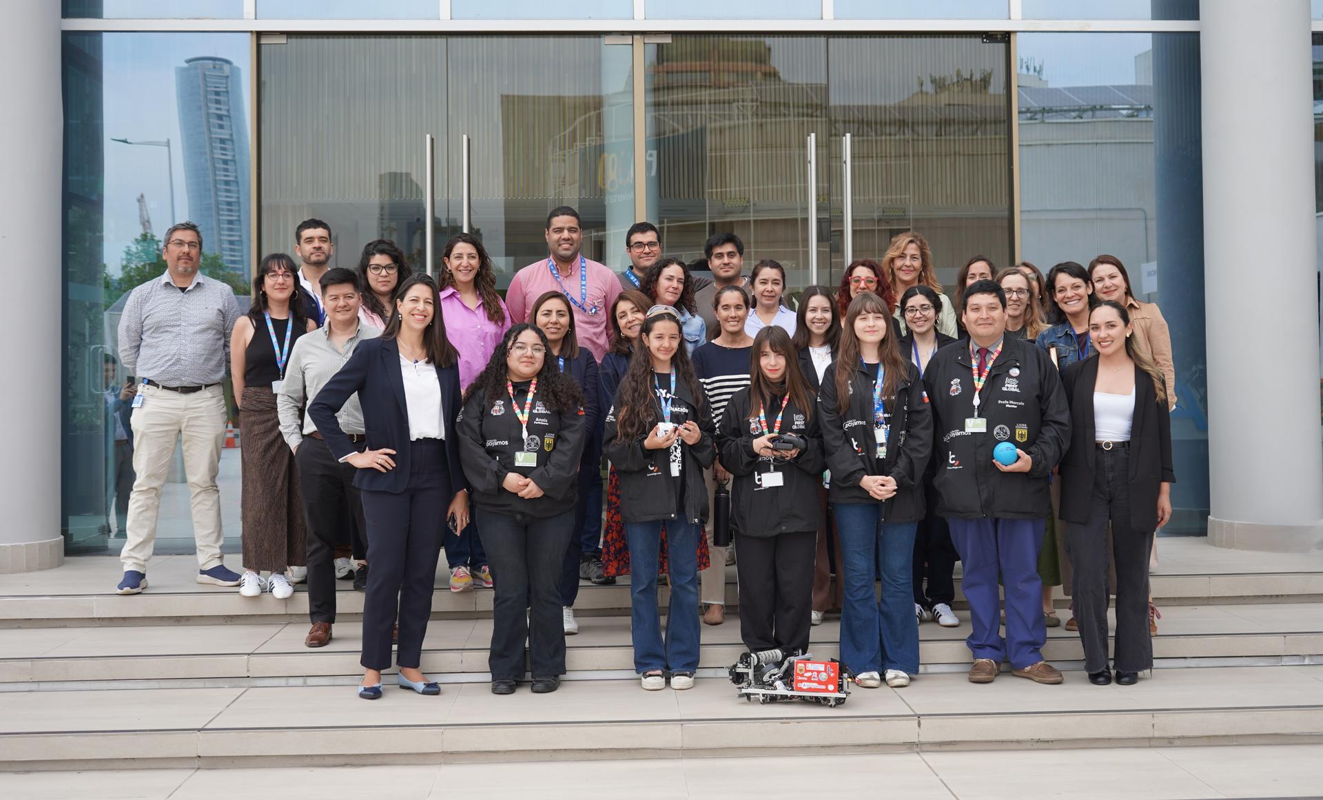 Group of diverse people posing on steps outside a modern glass-front building.