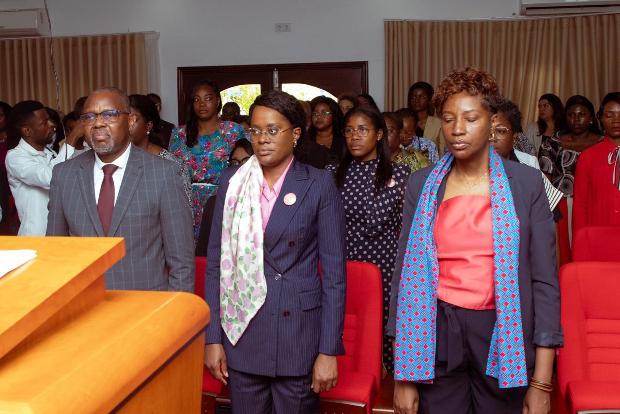 Photograph of formally dressed people standing in a hall with a wooden podium at the front.