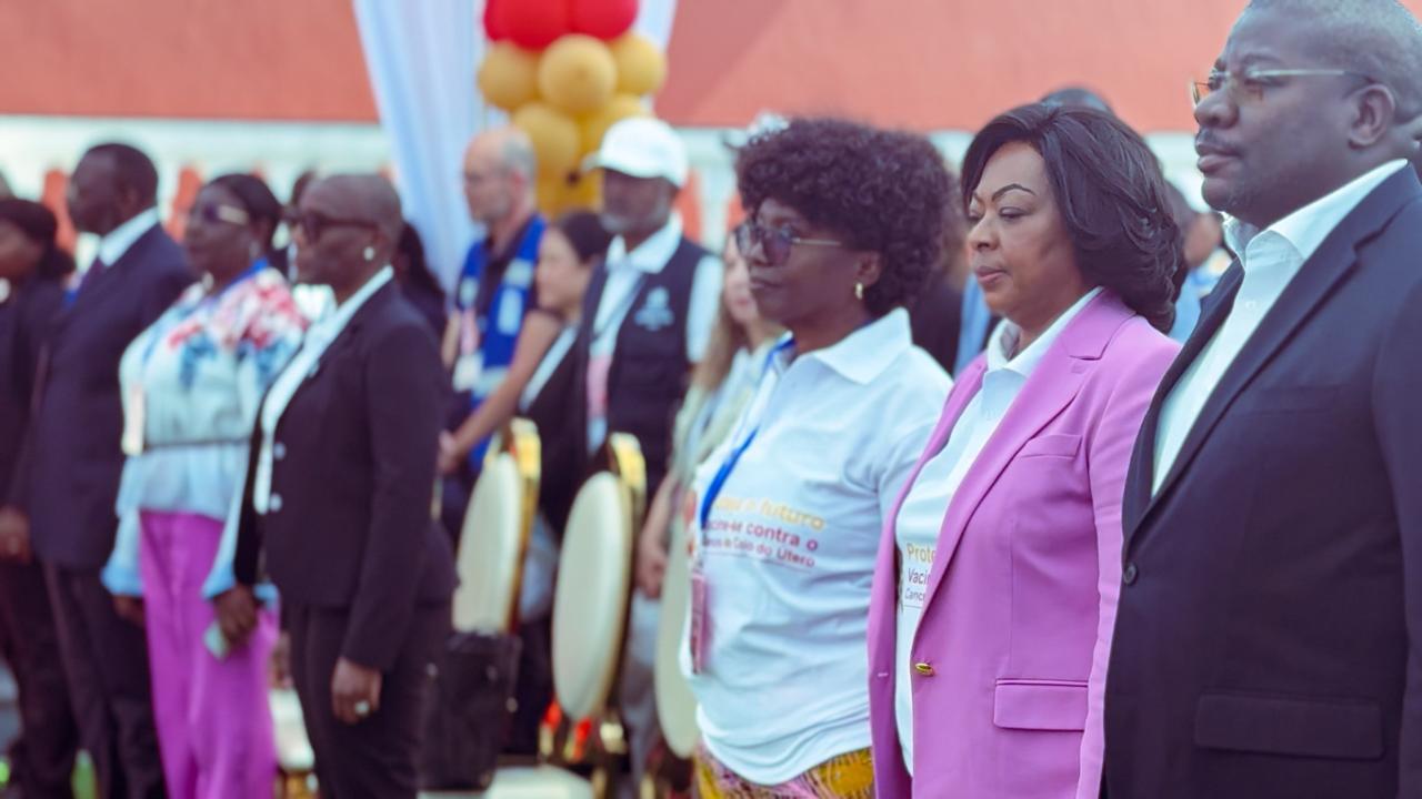 Line of formally dressed people wearing lanyards at an outdoor event with balloons.