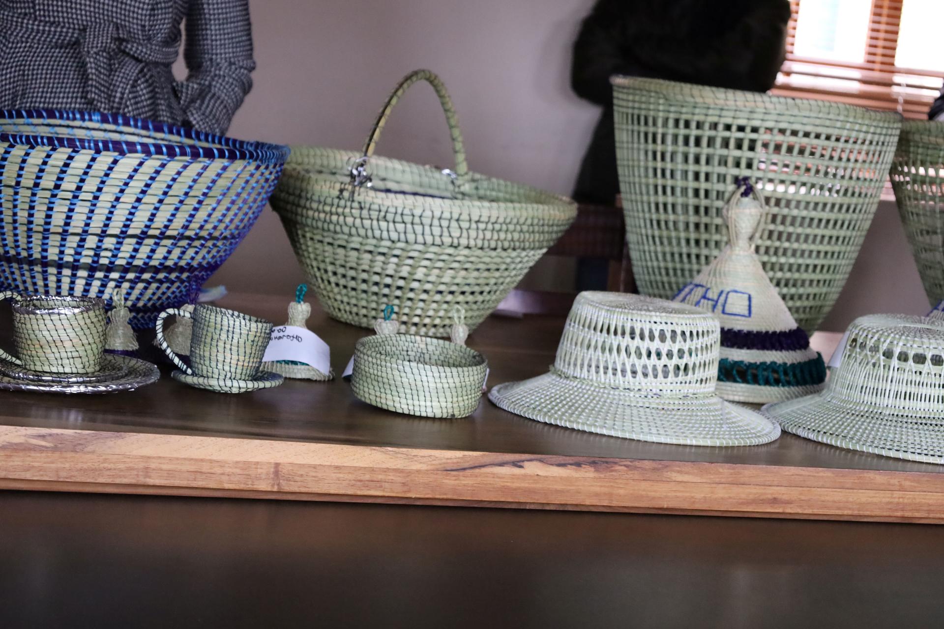 Assorted woven baskets on a wooden shelf, with small cups and a light straw hat.