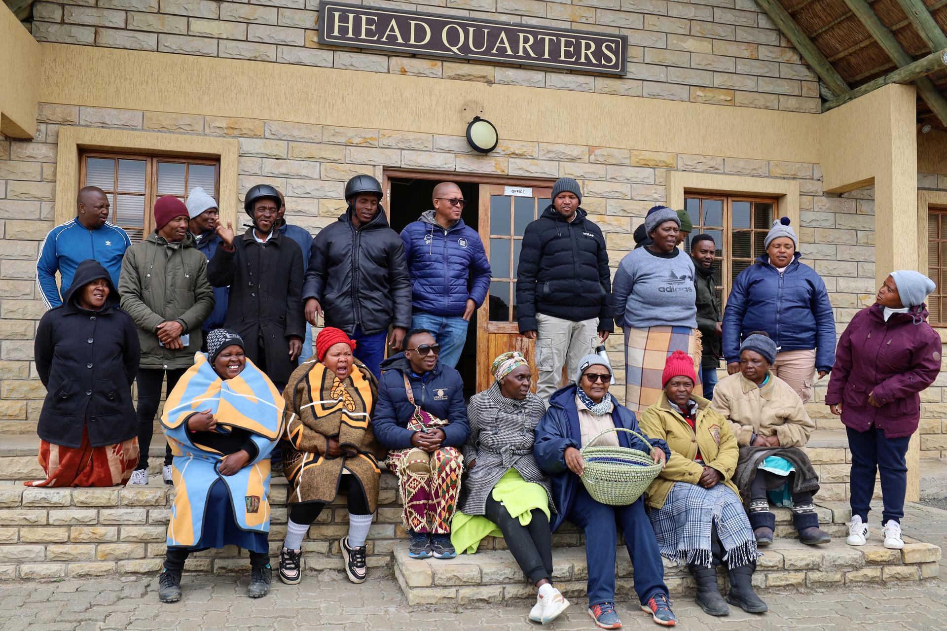 Group of people posed on the steps outside a beige building labeled HEAD QUARTERS.