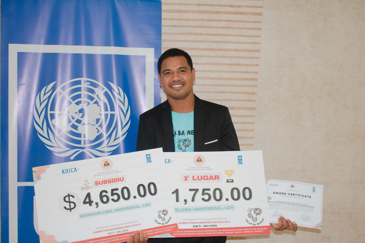 Person stands before a UN banner, holding two oversized checks totaling $6,400.