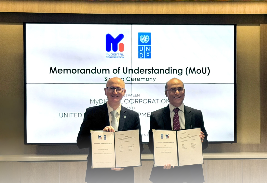 Two men in suits hold signed MoU documents during a formal signing ceremony.