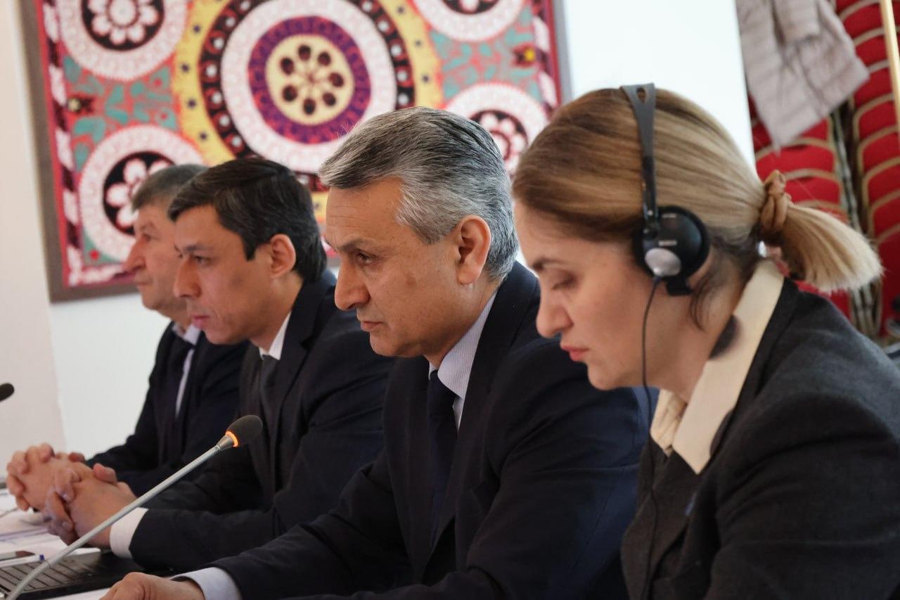 Four professionals in suits sit at a conference table, attentively listening.