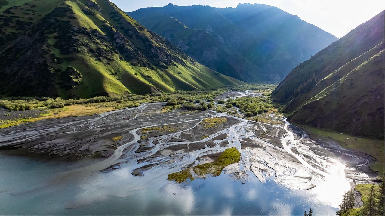Alpine valley with green slopes and a reflective river winding between mountains.