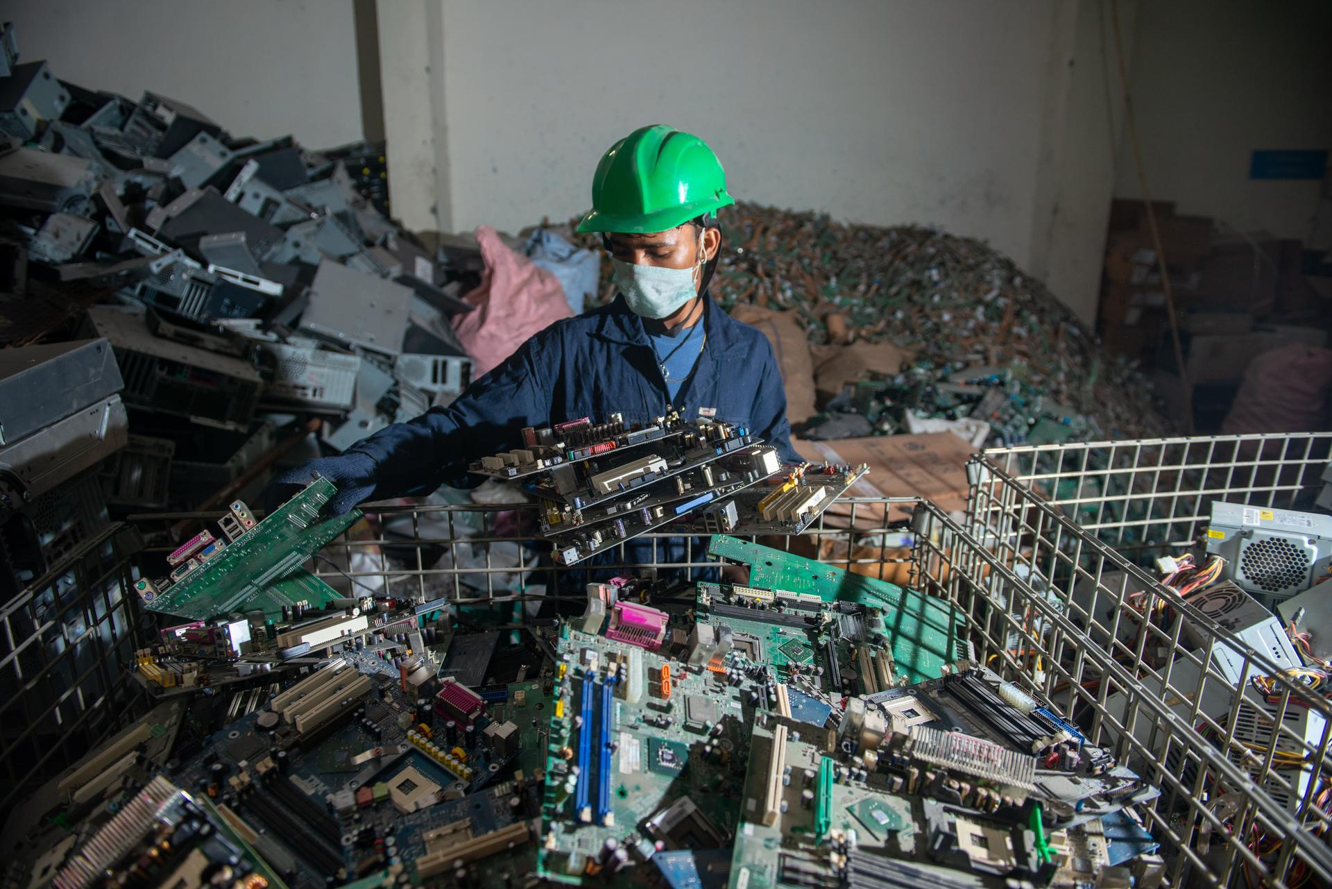 Worker in blue jacket and green safety helmet among piles of scrap metal.