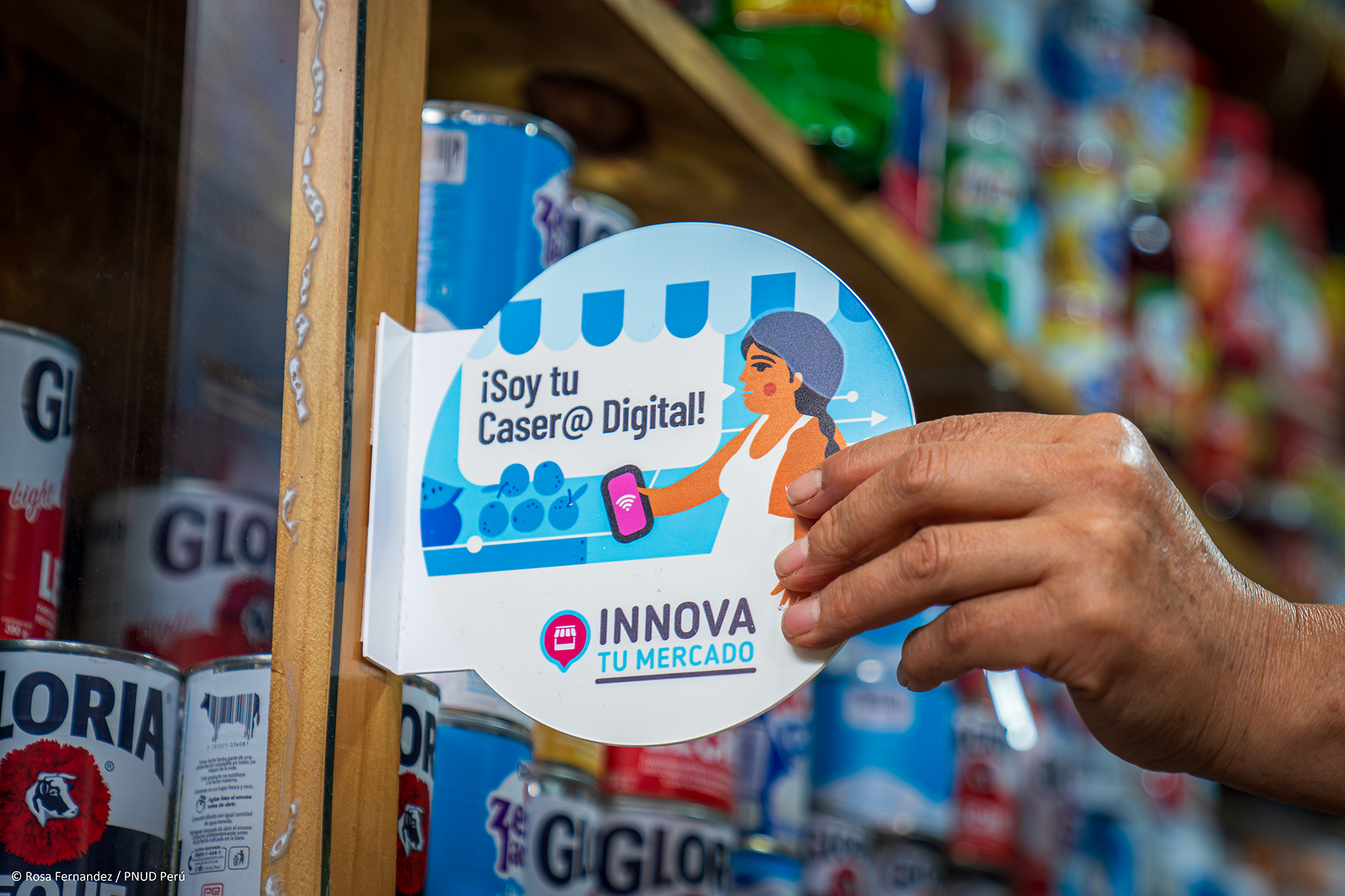 Hand holding round blue promo card with a photo and INNOVA branding in a store aisle.