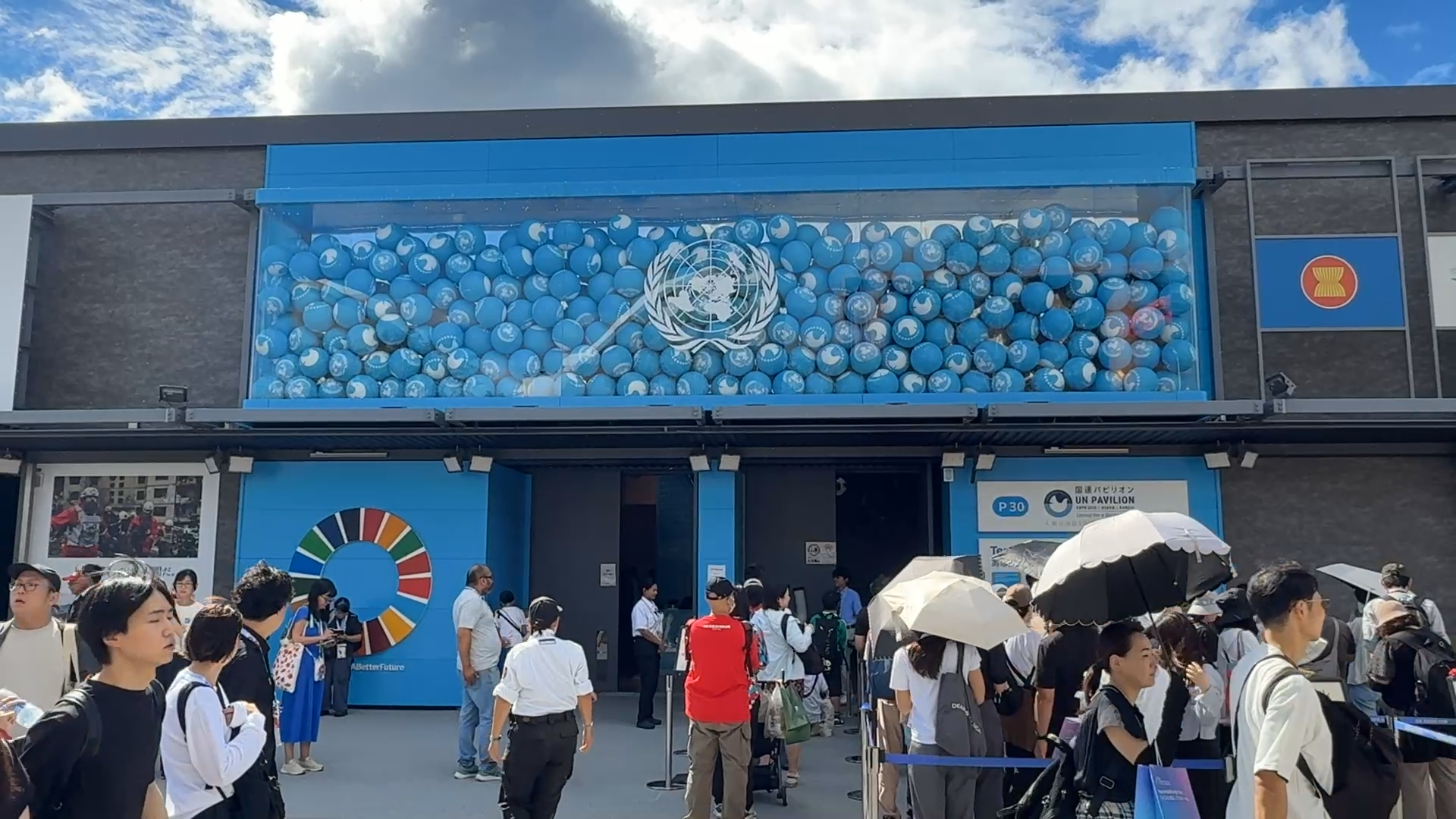 Blue building facade with a circular emblem, crowd of people outside on a sunny day.