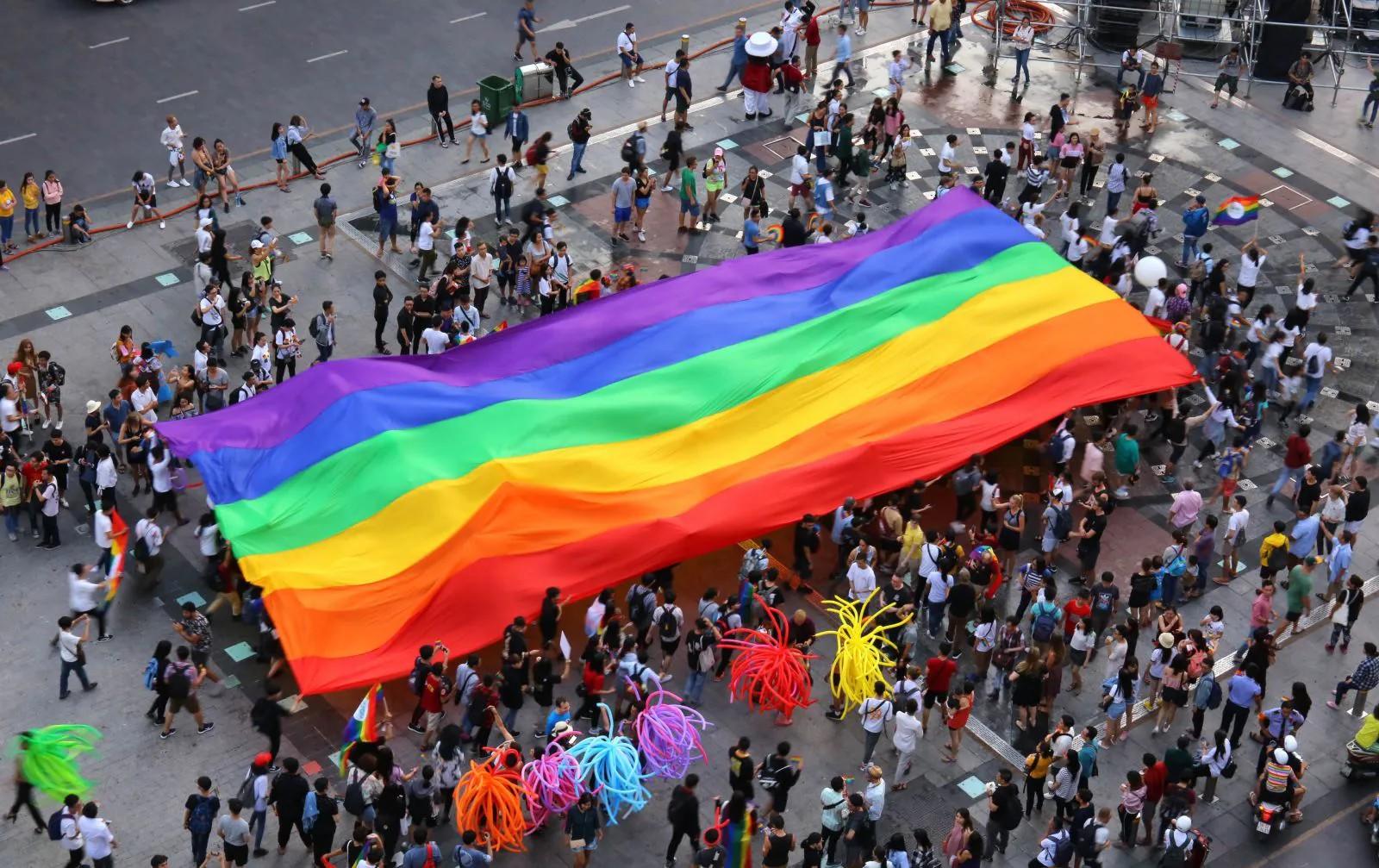 Photograph: aerial view of a large rainbow flag over a crowd at a Pride event.