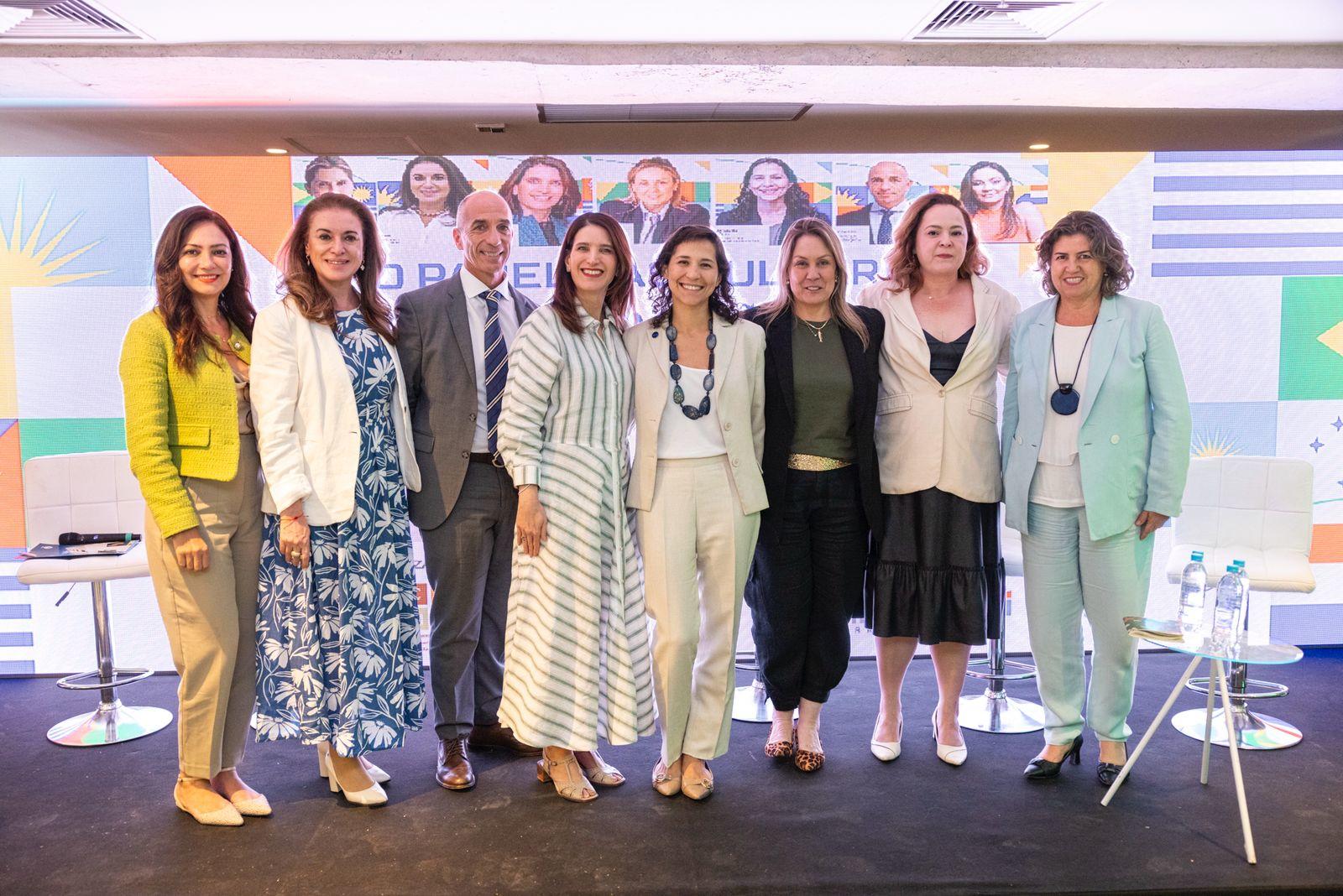 Diverse group of professionals posing on a conference stage with a pastel backdrop.
