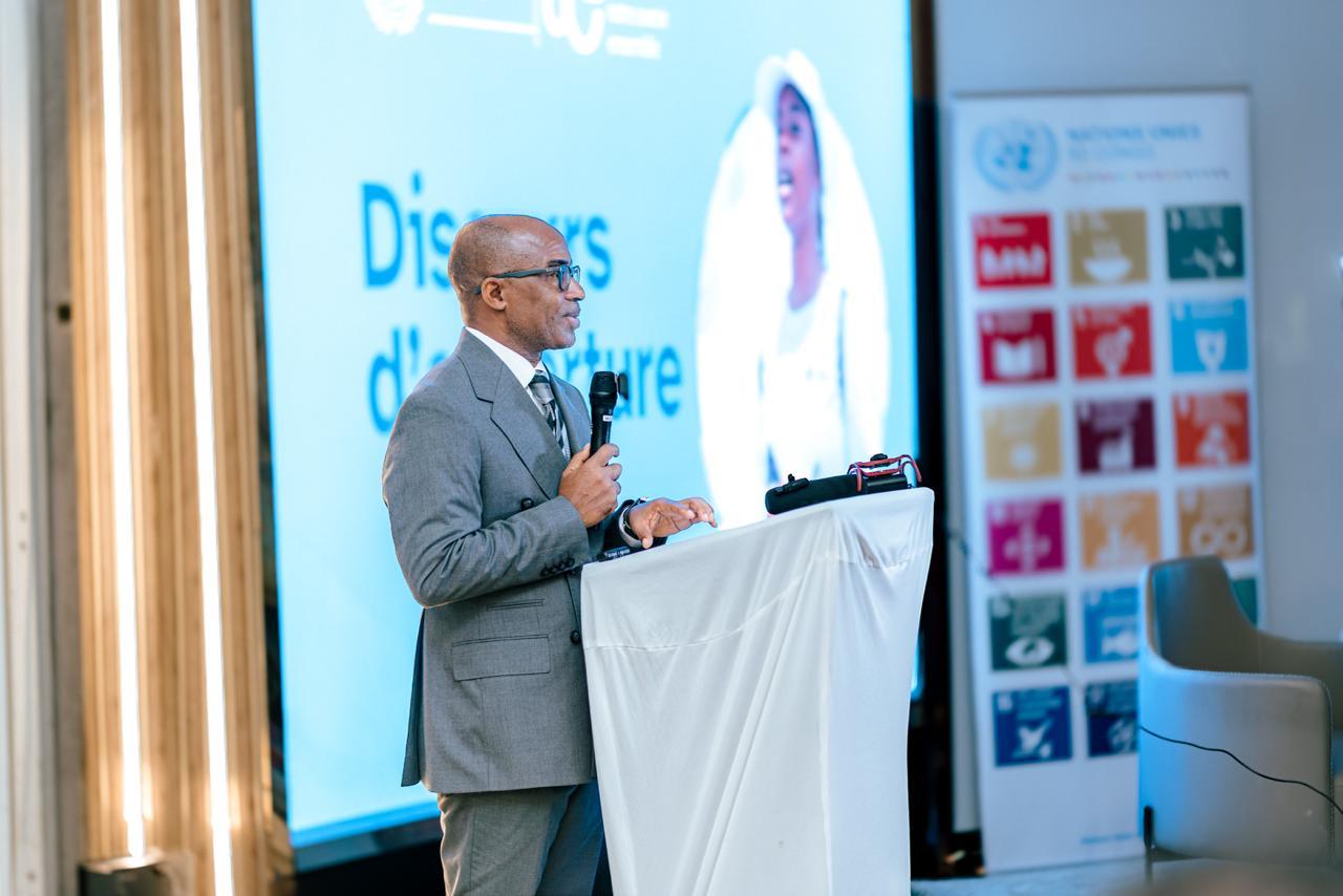 Photograph of a man at a podium giving a presentation at a conference, with blue slides behind.