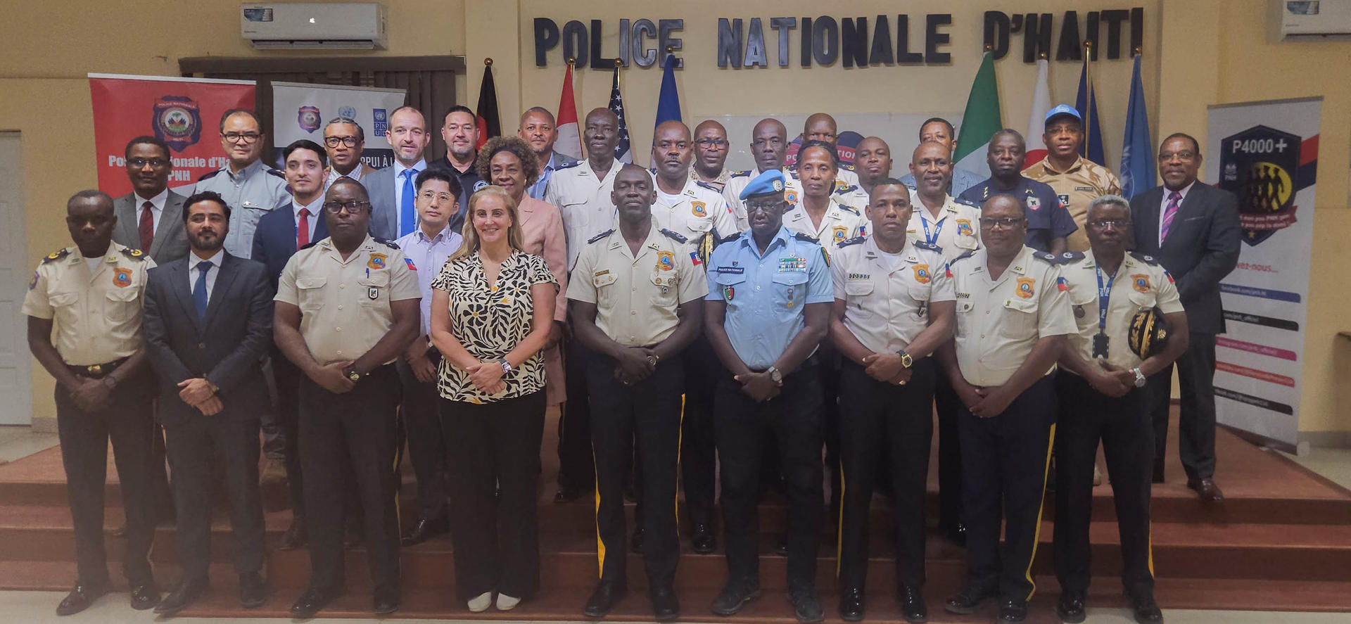 Group of police officers and civilians posing indoors in front of a Police Nationale d'Haïti banner.