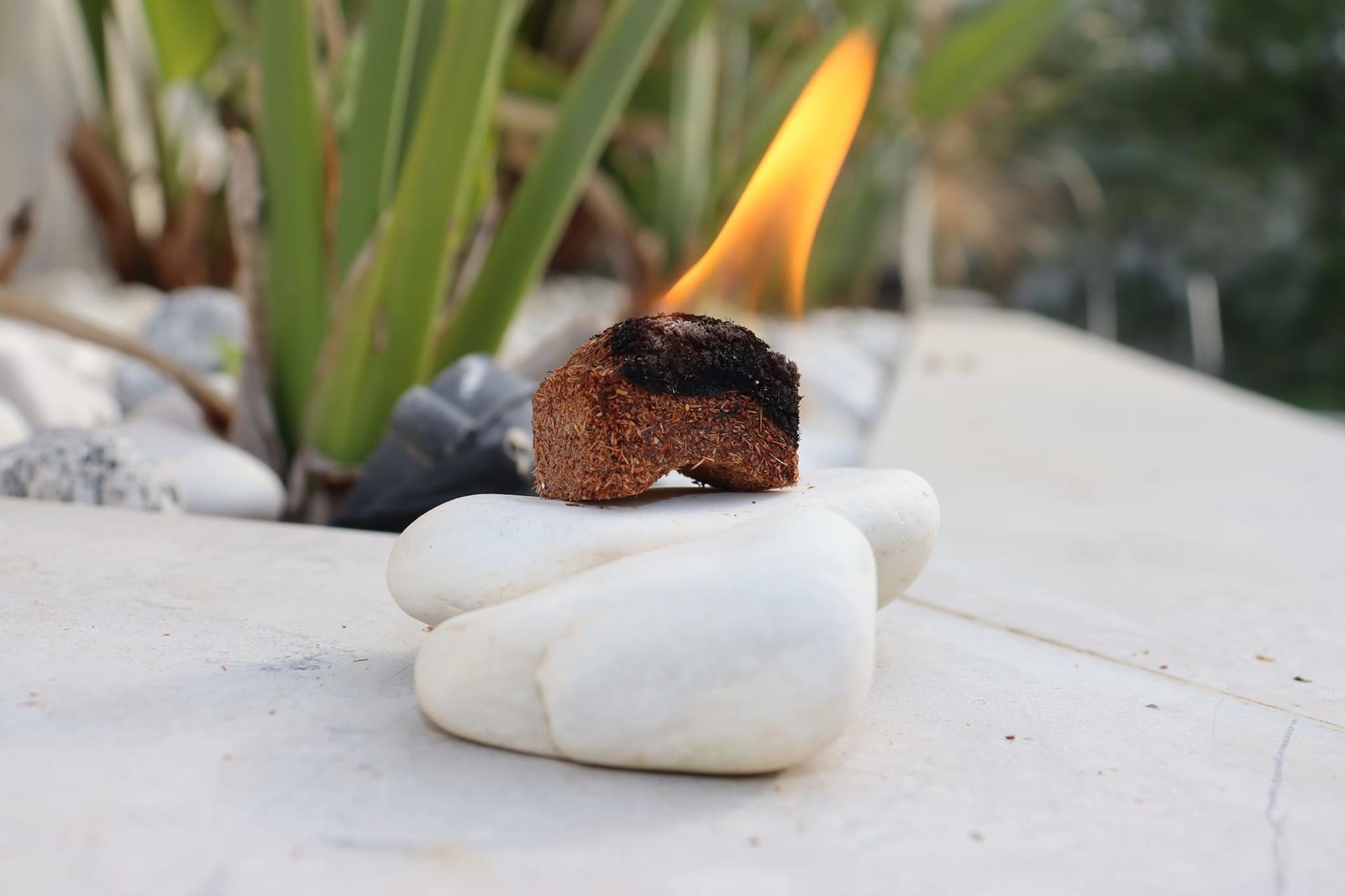 Small flame above a dark rock balanced on smooth white stones in a garden.