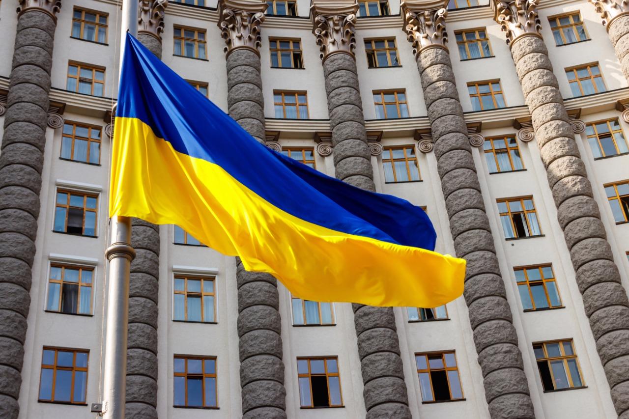 Ukrainian flag fluttering in front of a grand stone government building.