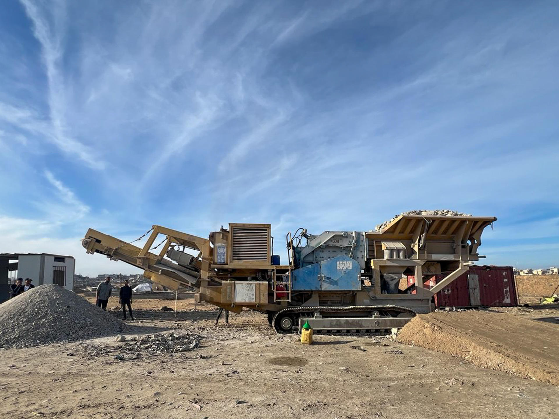Construction site with a large excavator and dirt piles under a blue sky.
