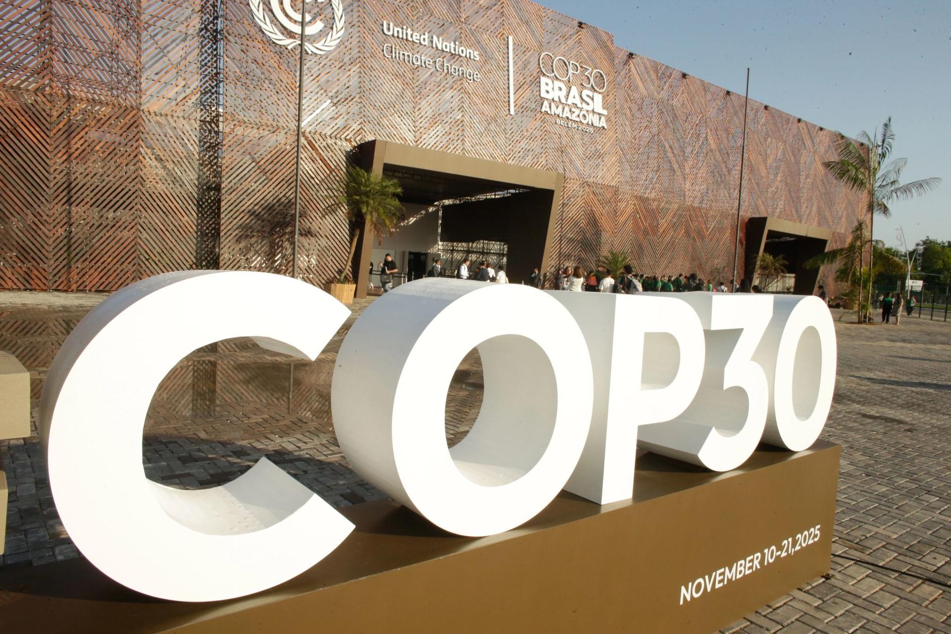 Large white COP30 letters sculpture in front of a conference venue.