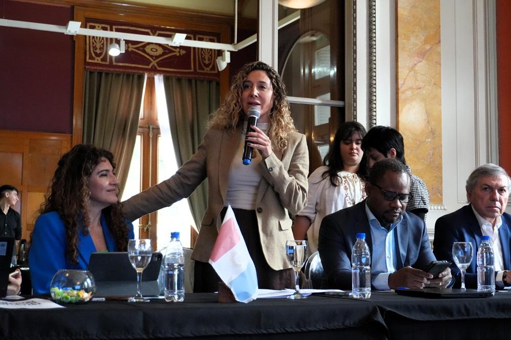 Speaker at a conference table addressing attendees; small French flag on the table.